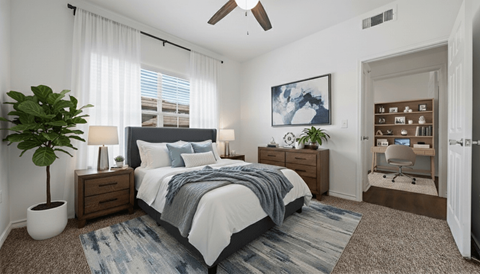 A bedroom with a bed, a plant, a ceiling fan, and a painting on the wall.