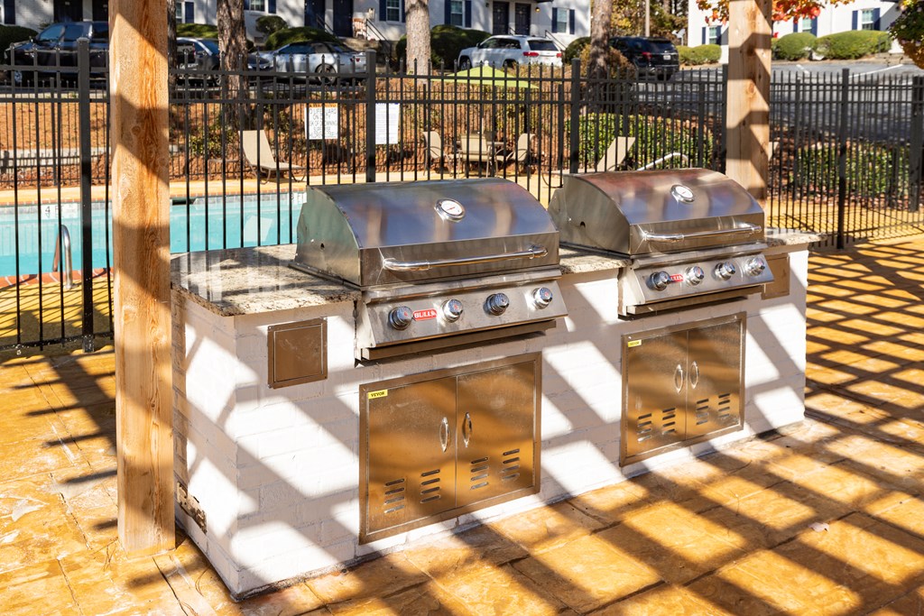 two bbq grills on a patio with a pool in the background