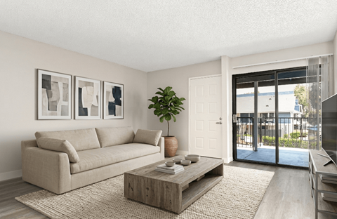 A living room with a beige couch, a wooden coffee table, and a plant.