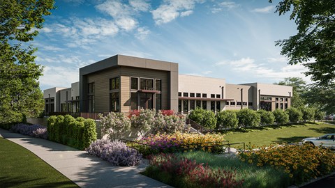 A modern building with a grey facade and large windows is surrounded by a well-manicured garden with a variety of colorful flowers.