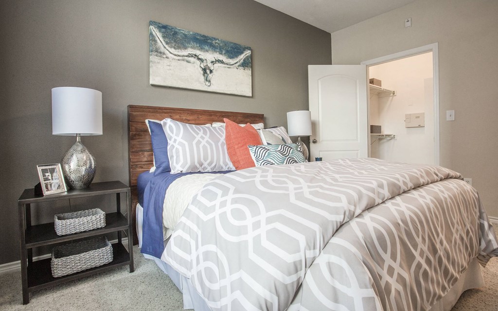 A bed with a white and grey patterned comforter and a blue pillow with a wooden headboard.