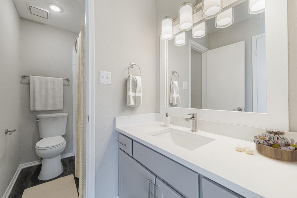 A white toilet is in a bathroom with a white sink and a mirror.