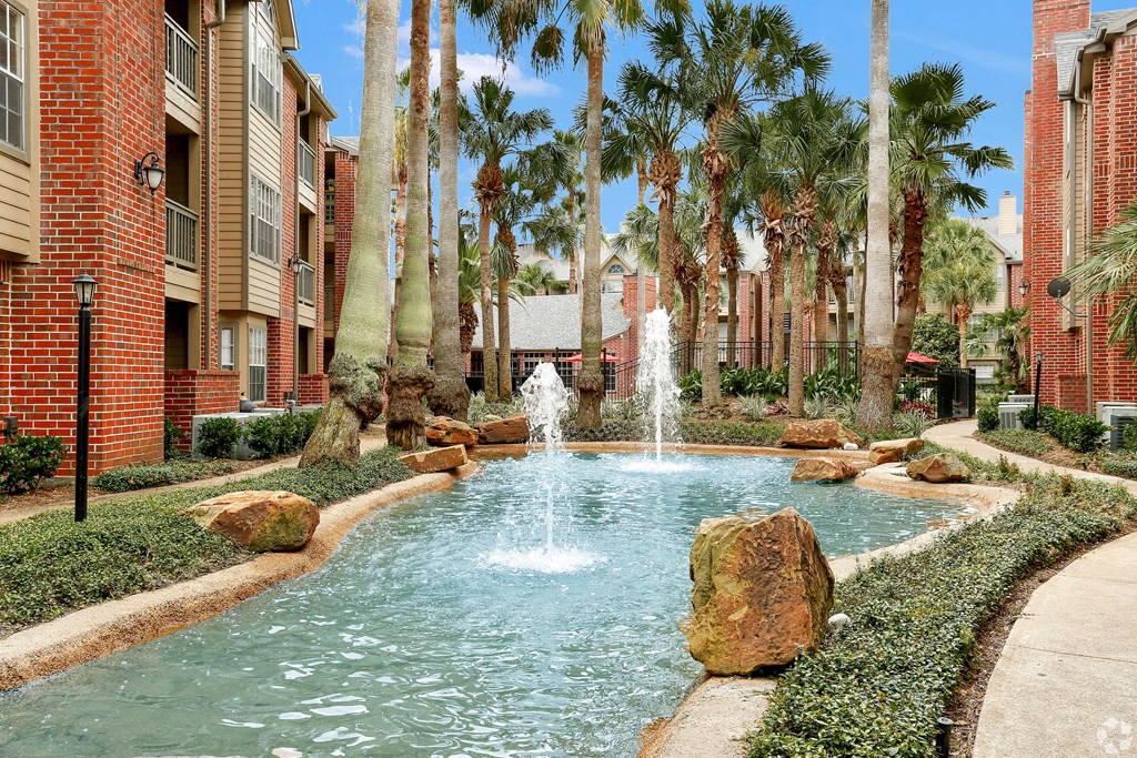a fountain in the middle of a pool with palm trees