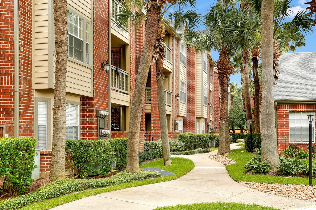a sidewalk in front of an apartment building with palm trees