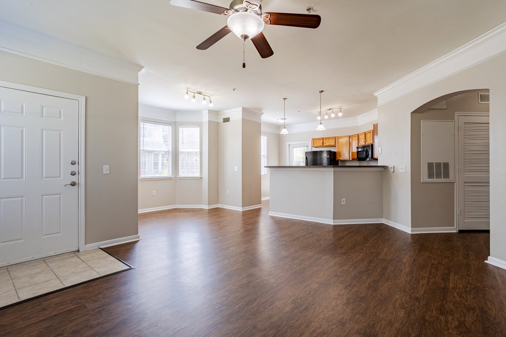 an empty living room with a ceiling fan and a kitchen