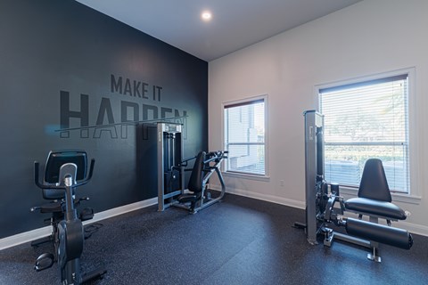 A gym with a wall that says "make it happen" and a row of exercise equipment.
