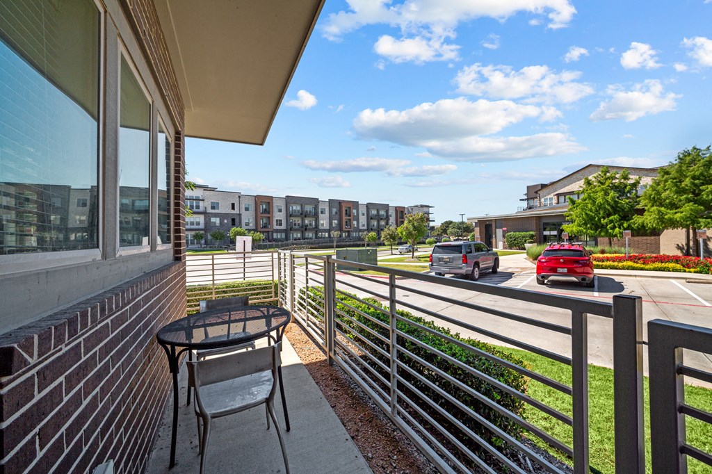 A balcony with a table and chairs overlooks a street with cars and buildings.