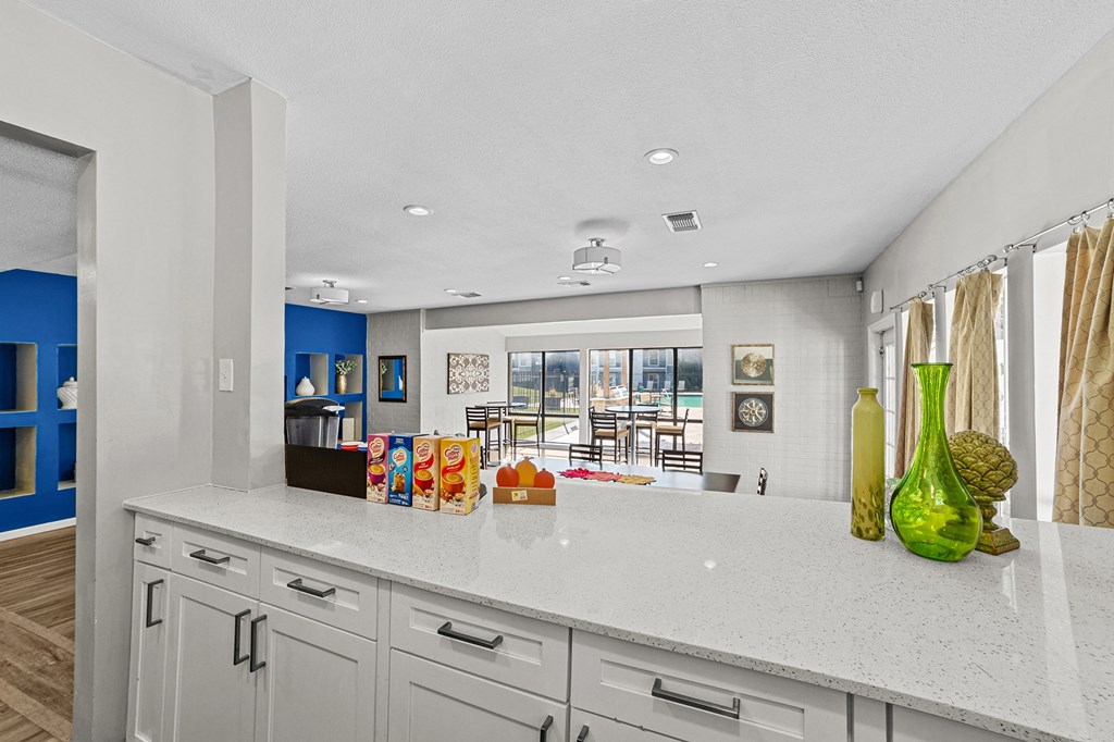 A kitchen with white cabinets and a white countertop with a green vase on it.