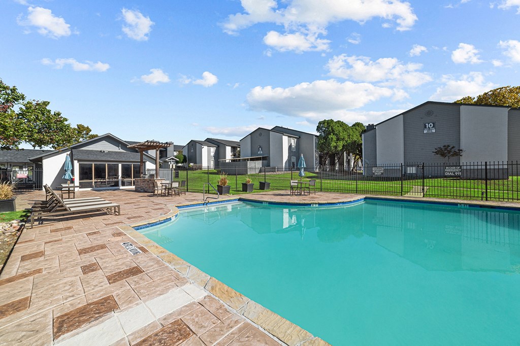 A swimming pool surrounded by a brick patio and a black fence.