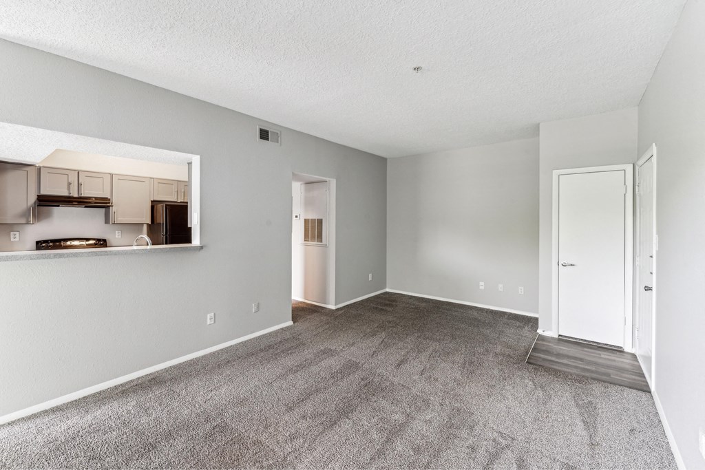the living room and dining room of an apartment with white walls and carpet