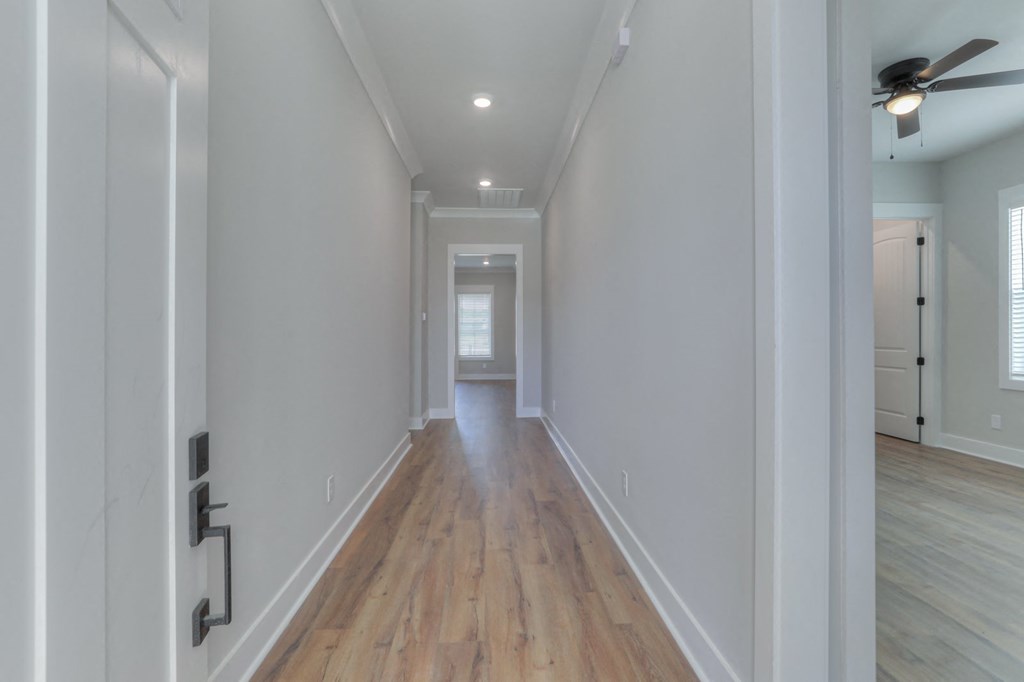 a long hallway with white walls and wood floors and a ceiling fan