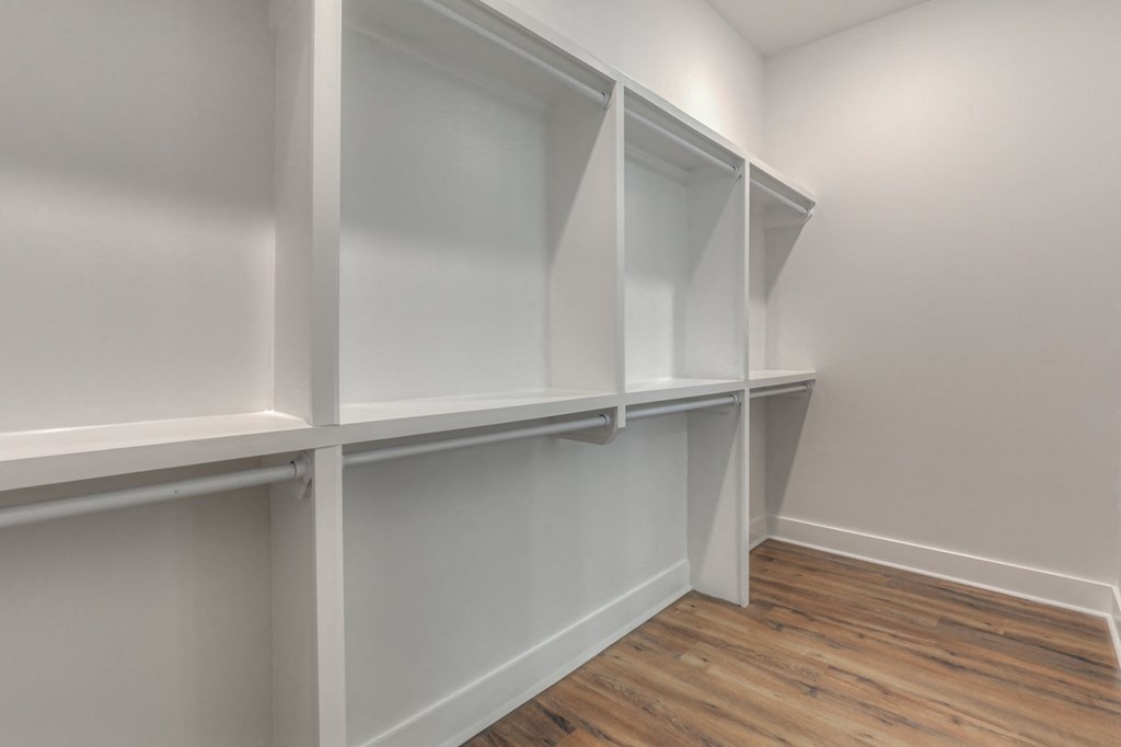 a walk in closet with white shelves and a wood floor