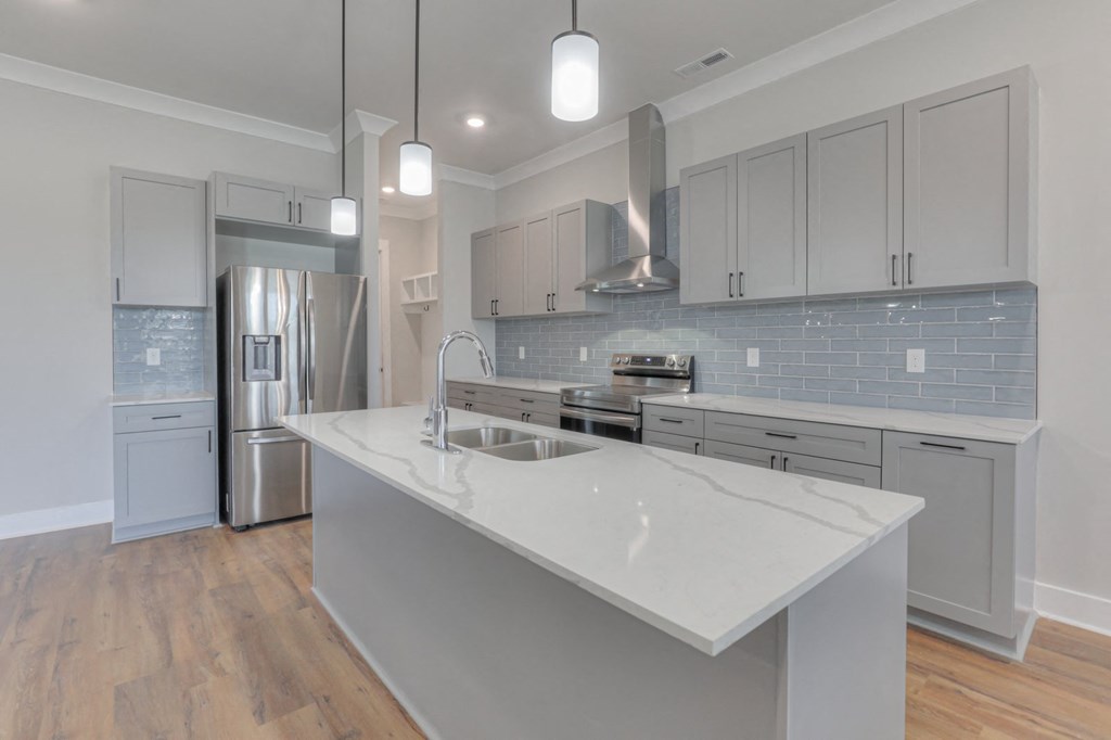 a white kitchen with a large island and a stainless steel refrigerator