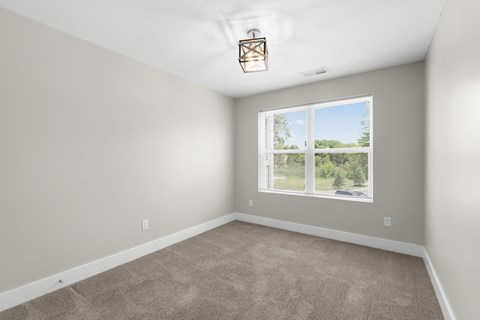 A room with a carpeted floor and a window showing a view of trees and a house.