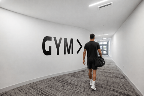 A man walking in a hallway with a Gym sign on the wall.