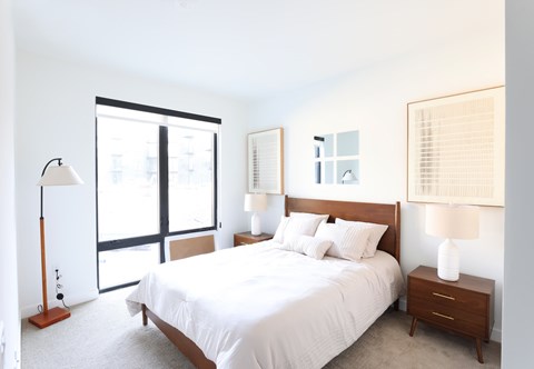 A bedroom with a large bed, a nightstand, and a floor lamp.