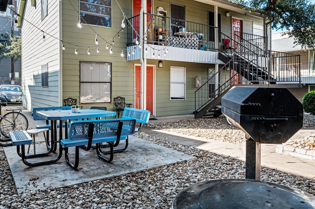 a patio with a table and chairs and a grill in front of a house