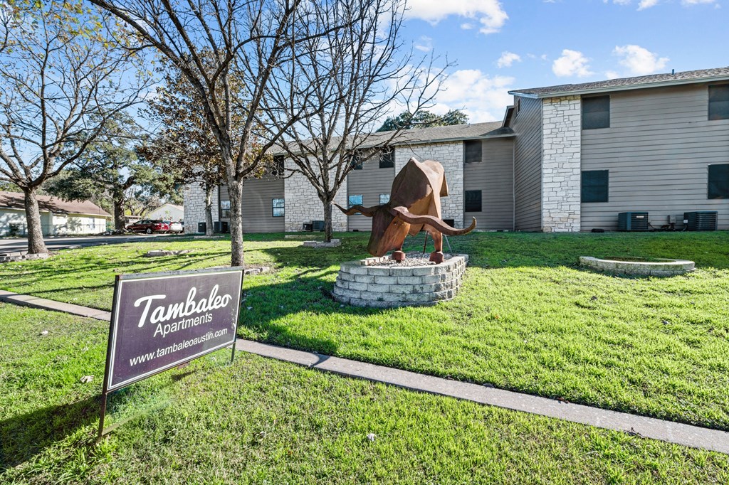 a statue of a bull in the grass in front of a building