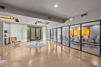 A modern office space with a glass wall and a table surrounded by chairs.
