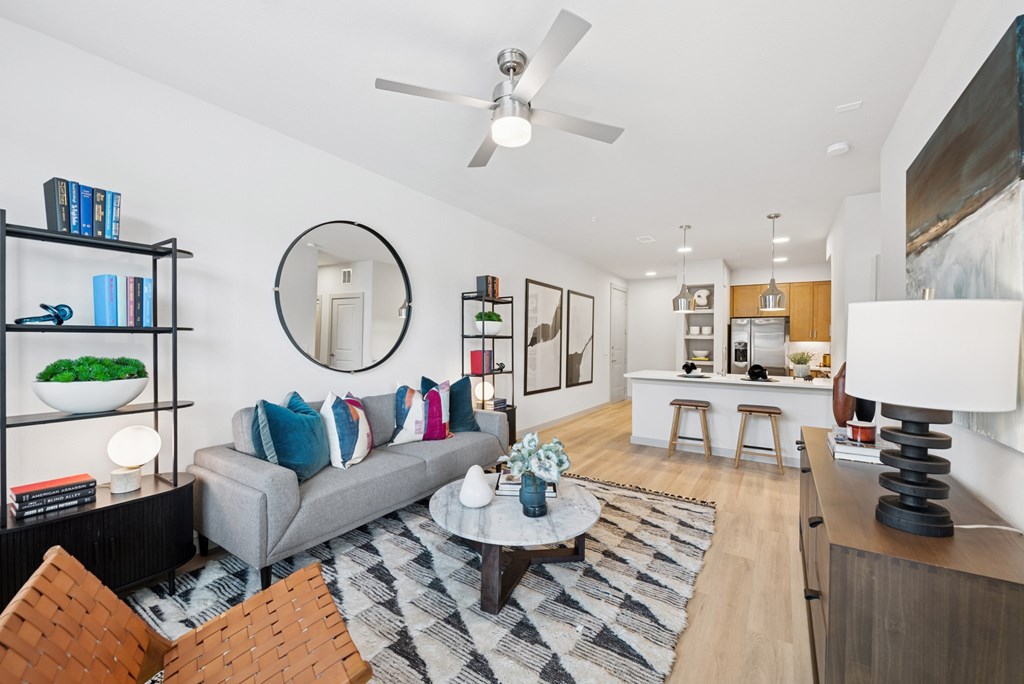 A living room with a grey couch and a round mirror on the wall.