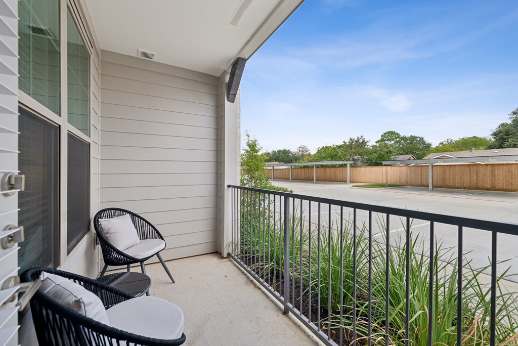 A balcony with a chair and table overlooking a fence.