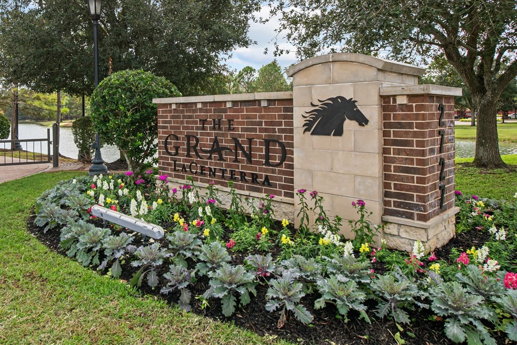 a brick sign with a black horse on it next to a flower garden