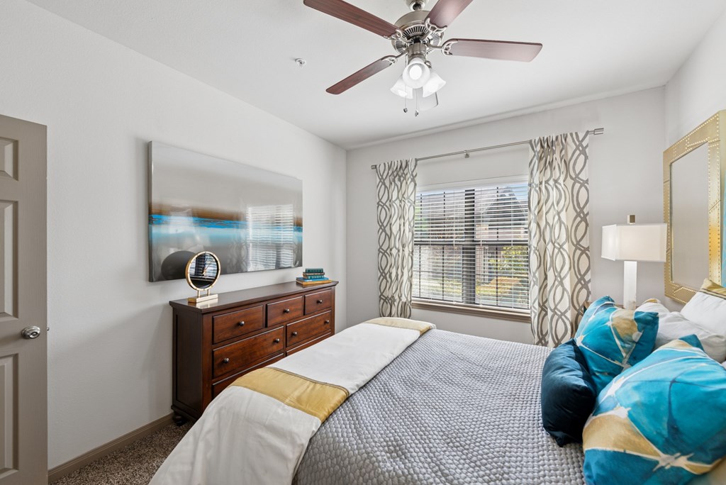 A bedroom with a bed, dresser, and a ceiling fan.