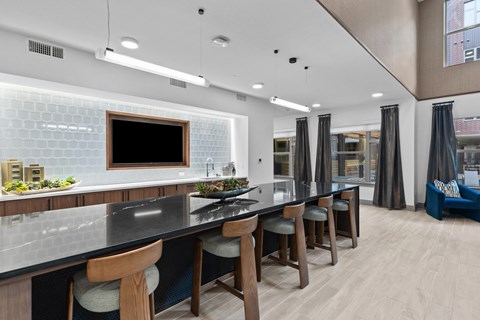 A modern kitchen with a long black counter and wooden chairs.