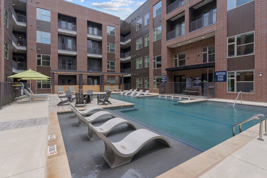 a swimming pool with chaise lounge chairs in front of an apartment building