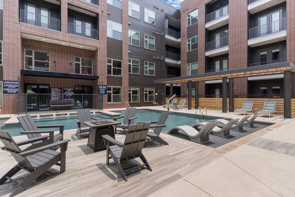 a pool area with lounge chairs and tables in front of an apartment building