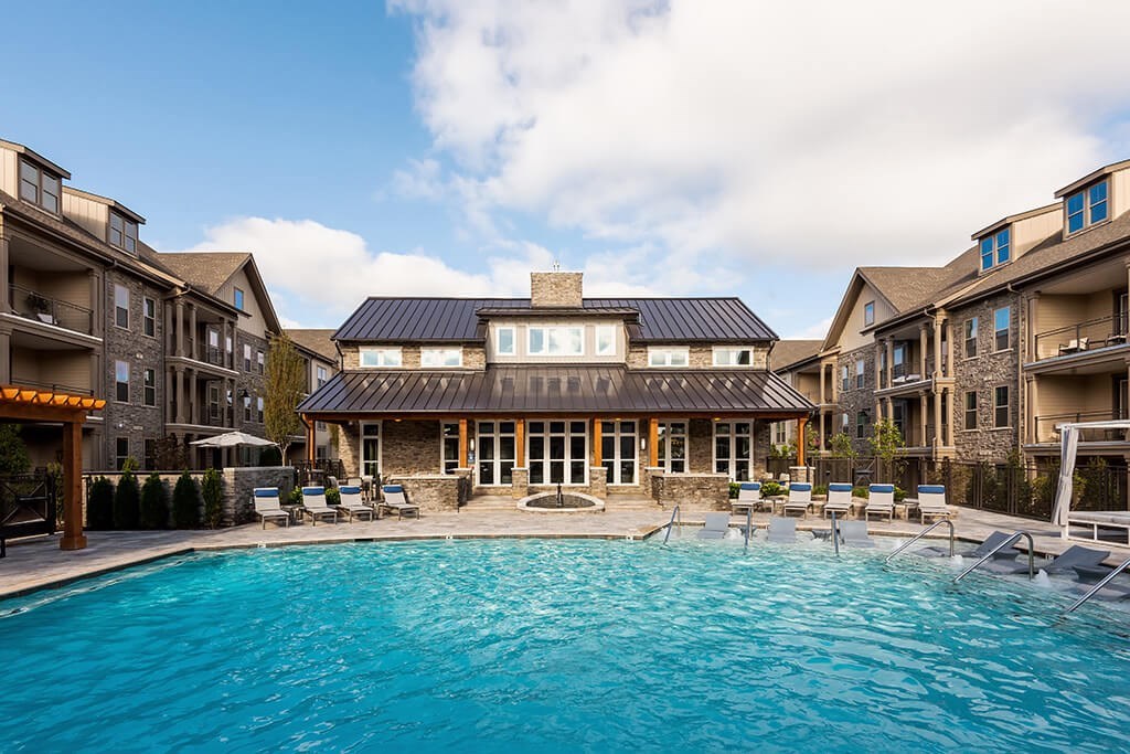 A large swimming pool in front of a building with a covered patio area.