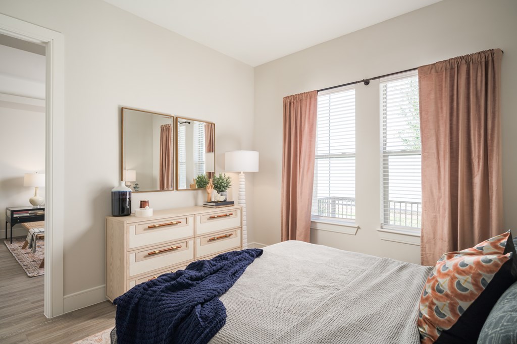 A bedroom with a bed, dresser, and window with curtains.