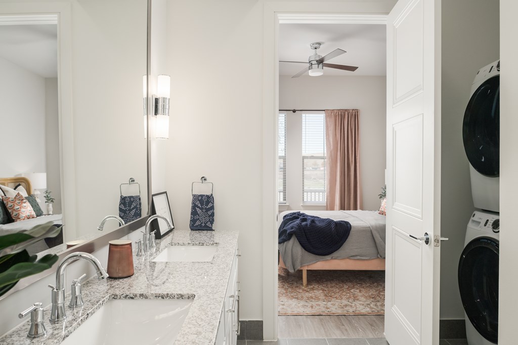 A modern bathroom with a double sink vanity and a view into a bedroom.
