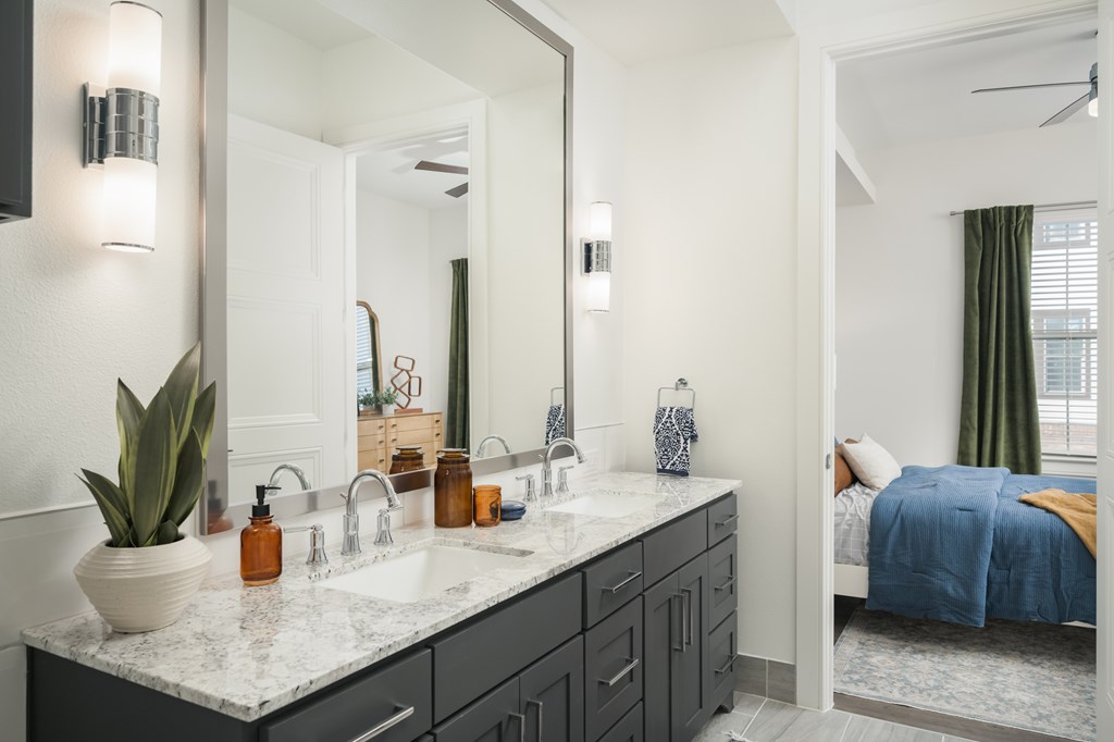 A bathroom with a large mirror, a sink, and a bed in the background.