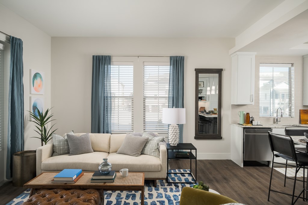 A modern living room with a white sofa, a wooden coffee table, and a kitchen area in the background.