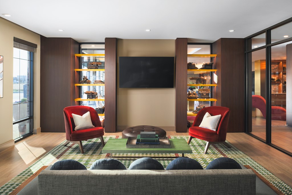 A living room with a grey sofa, red chairs and a black television.