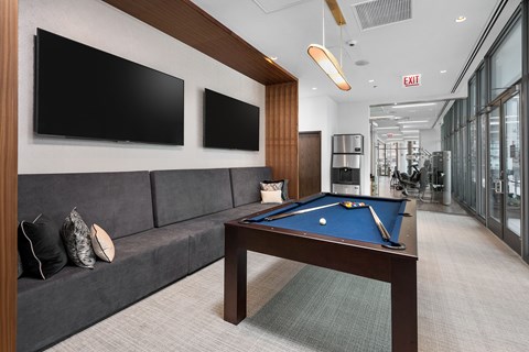 A pool table in a room with a couch and two TVs.