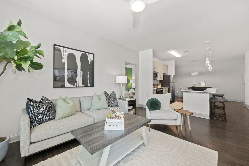 a living area with a couch coffee table and chairs and a kitchen in the background