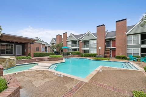 A swimming pool surrounded by brick and tile walkways in front of apartment buildings.