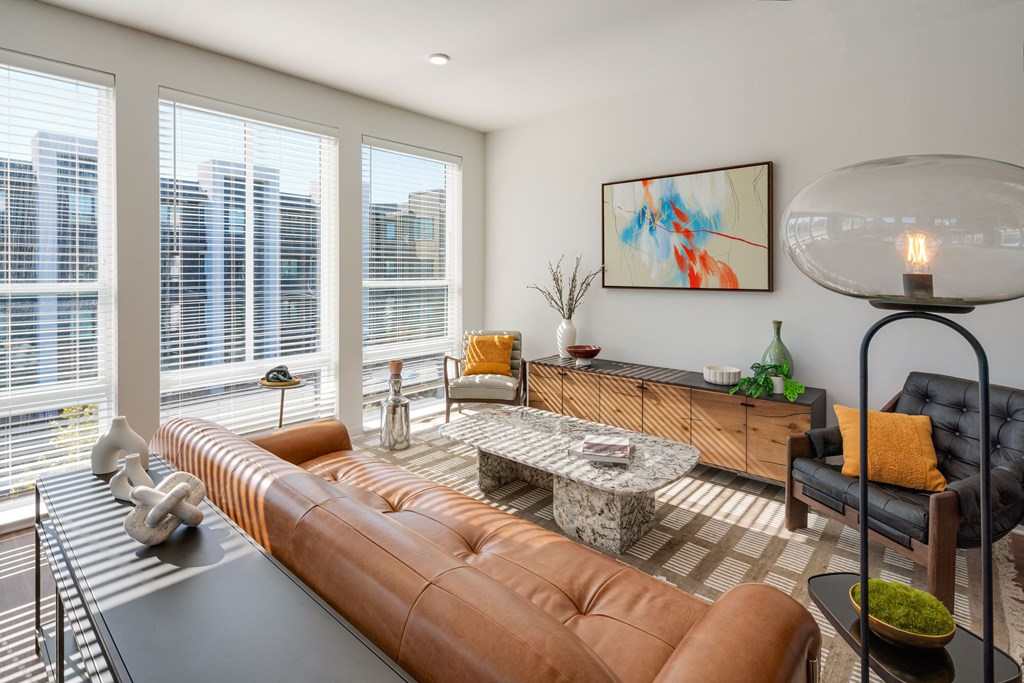 A modern living room with a brown leather sofa and a large window overlooking a cityscape.