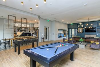 A pool table is in the middle of a room with a bar and a couch.