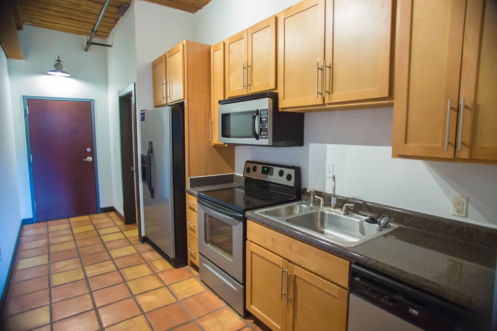 A kitchen with brown cabinets and a black fridge.