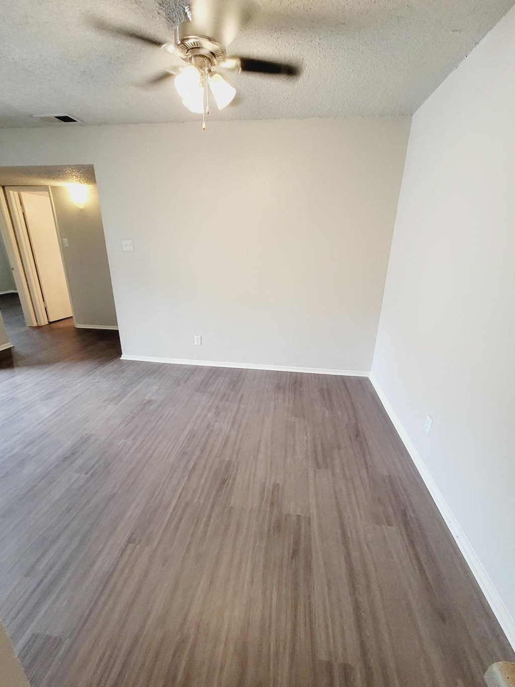 an empty living room with wood floors and a ceiling fan