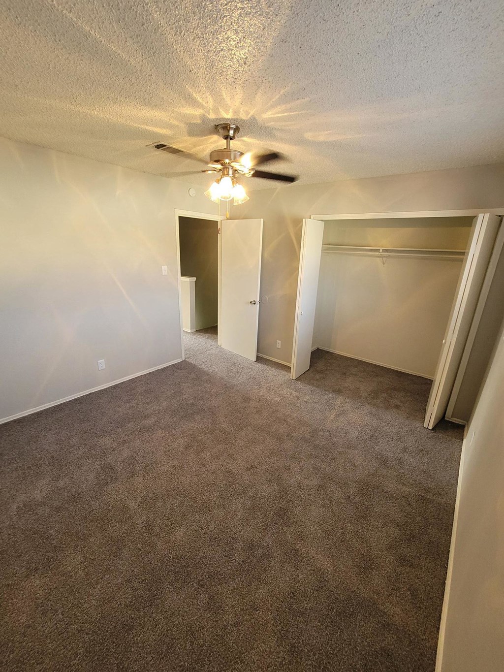an empty living room with a ceiling fan and empty closets
