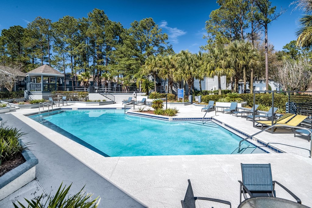 A swimming pool surrounded by trees and chairs.