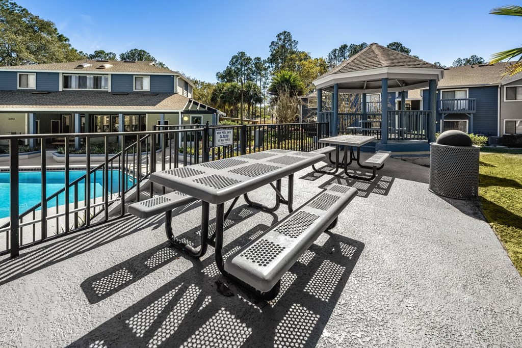A picnic table and benches are set up on a patio next to a pool.