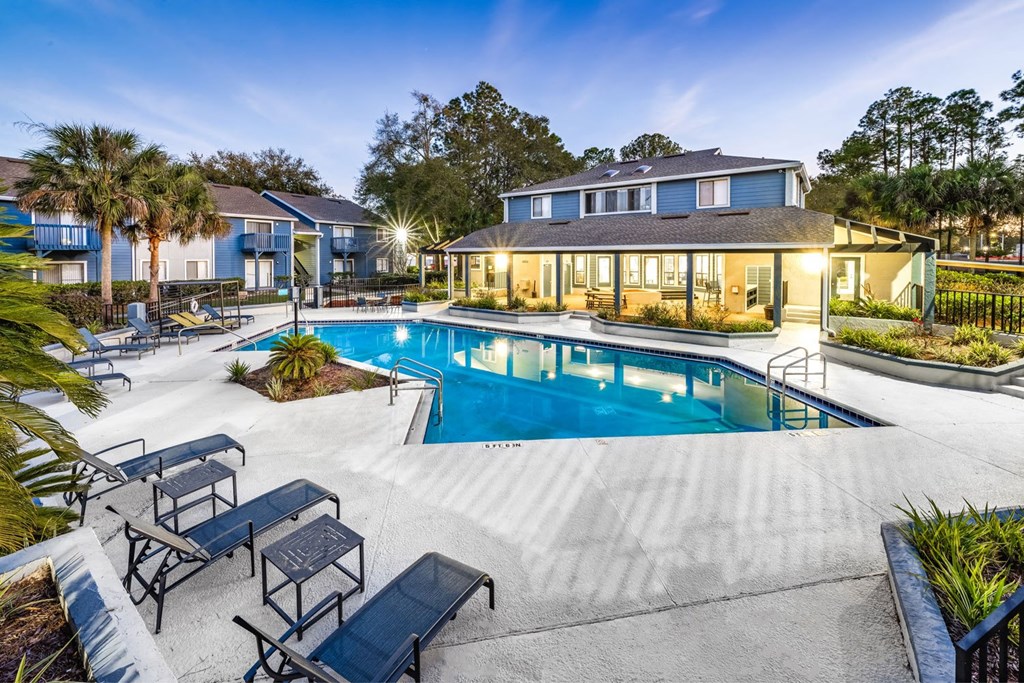 A swimming pool surrounded by a concrete patio and lounge chairs.