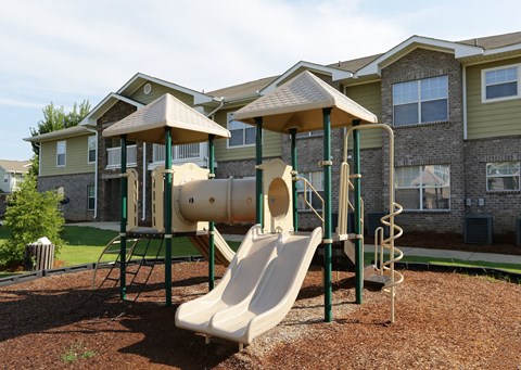 A playground with a slide and a tunnel in front of apartment buildings.
