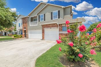 A house with a driveway and a rose bush in front.