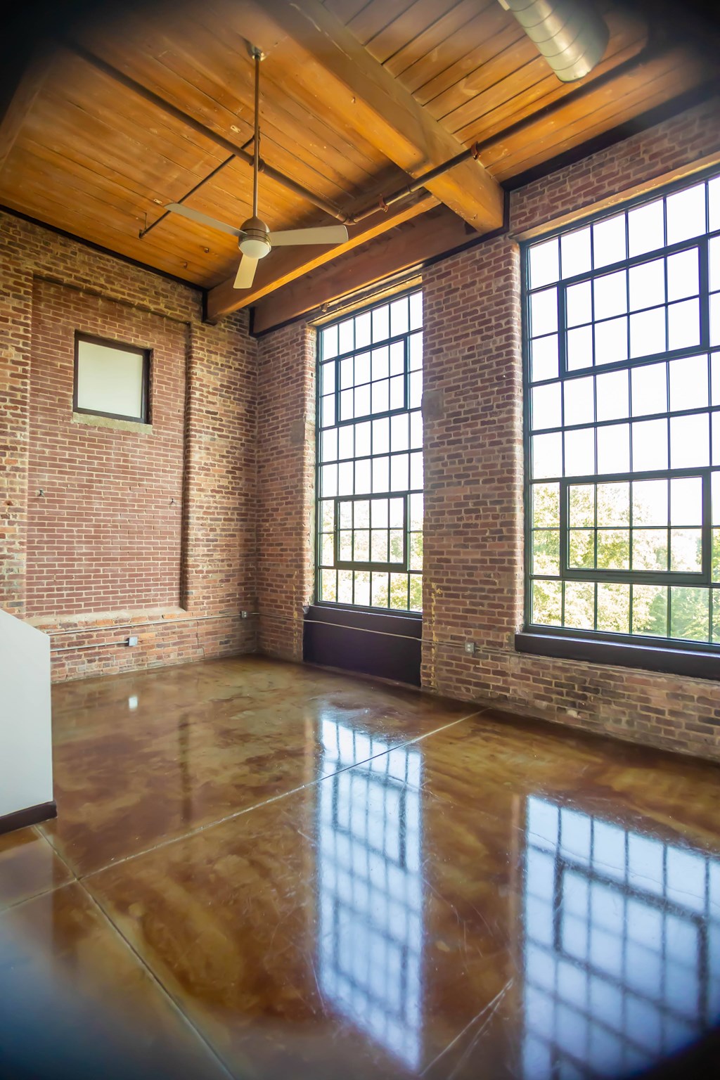 A room with a ceiling fan and large windows.
